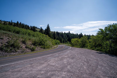 Country road amidst trees against sky