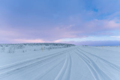 Tire tracks on snow covered road in an arctic landscape under a cloudy evening sky