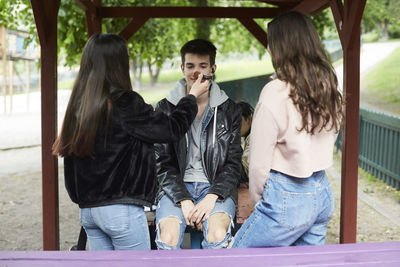 Female friends applying make-up to male teenager