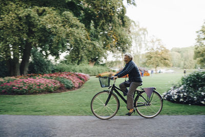 Full length side view of smiling senior woman riding bicycle in park