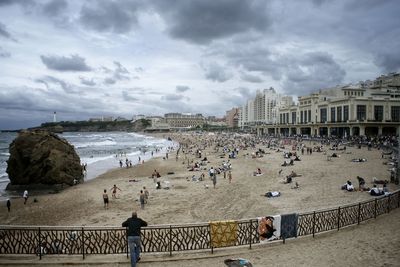 Crowd at beach against cloudy sky in city