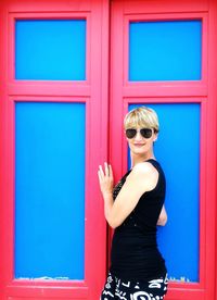 Side view portrait of woman standing by closed red and blue doors