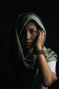 Portrait of young woman covered with scarf against black background