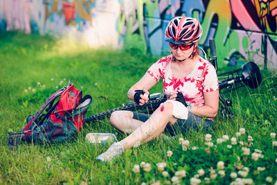 Injured female cyclist applying medicine on wound while sitting at park