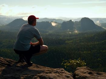 Hiker man take a rest on mountain peak. man sit on summit, bellow spring valley. sun shining in sky.