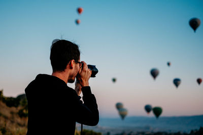 Man photographing with balloons against sky