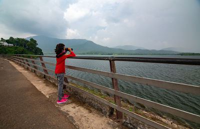 Rear view of woman standing by railing against sky