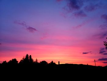 Silhouette trees against dramatic sky during sunset