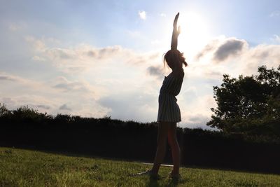 Woman with arms outstretched standing on field against sky