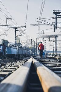 Rear view of man on railroad tracks against sky