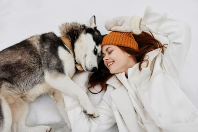 High angle view of smiling woman lying with dog on snow covered land