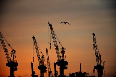 Silhouette cranes against sky at sunset