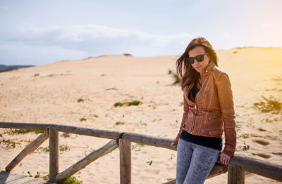 Woman wearing sunglasses while standing by railing against sky