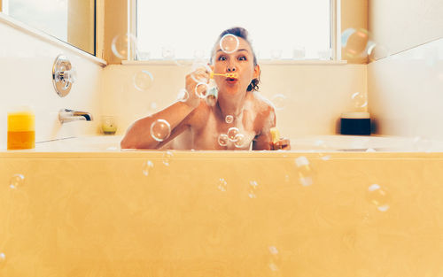 Portrait of woman blowing bubbles in bathroom