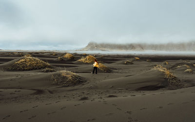 Man standing on sand dune in desert against sky