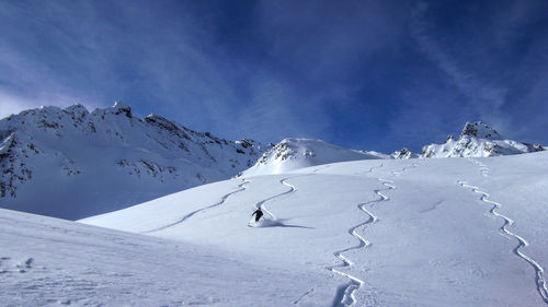 Person skiing on ski slope by snowcapped mountains against sky