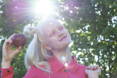 An albino girl in a red blouse against a background of green leaves and sunlight. 