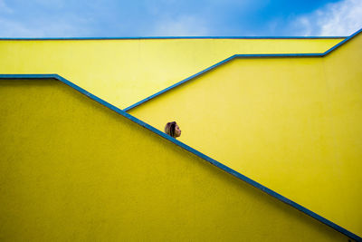 Low angle view of woman against yellow wall and sky