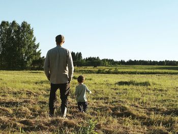 Rear view of father and son standing on field against clear sky