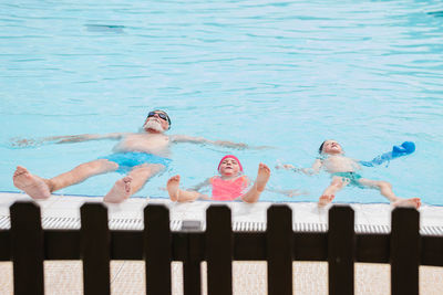 From above full body of adorable little sister and brother with bearded senior grandfather in swimwear floating in outdoor pool during summer holidays