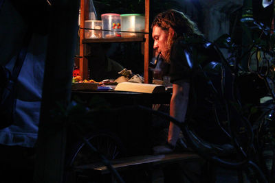 Side view of man reading book while sitting at market stall