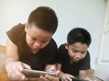 Siblings using mobile phones on parquet floor