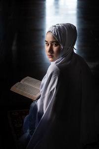 Portrait of young woman in hijab reading koran