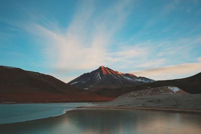 Scenic view of calm lake amidst mountains against cloudy sky during sunset