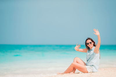 Young woman sitting on beach against clear sky