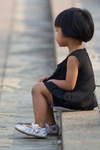 Side view full length girl sitting on retaining wall
