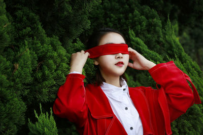 Young woman covering eyes with red strap against plants