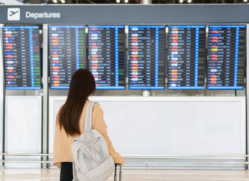 Woman looking at the flight information board, checking her flight at the airport traveling concept.