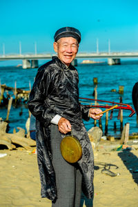 Woman holding musical instruments while standing at beach against sea and sky