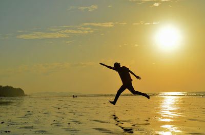 Silhouette man jumping at beach against sky during sunset