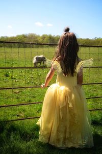 Rear view of girl in princess costume looking at pony on grassy field