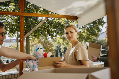 Portrait of smiling female volunteer packing stuffed toys in boxes with colleagues at community center