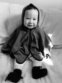 Portrait of cute baby girl sitting on bed at home