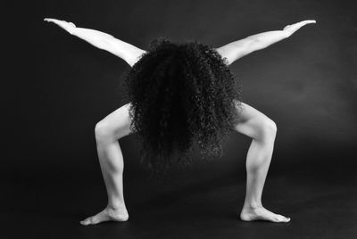 Naked woman with arms outstretched and curly hair standing against gray background
