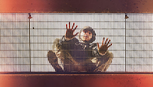 Portrait of man sitting over cage against sky