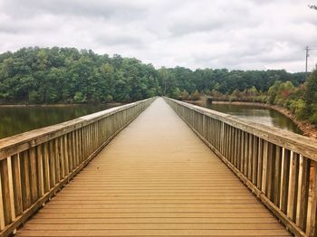 Footbridge amidst trees against sky