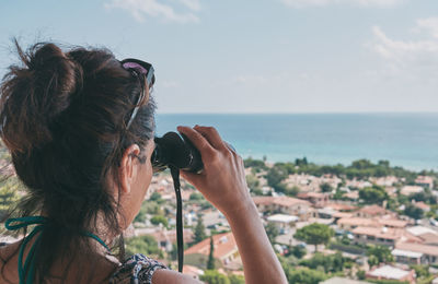 Portrait of woman photographing by sea against sky