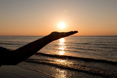 Silhouette hand against sea during sunset