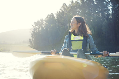 Smiling woman kayaking on lake against sky during sunny day