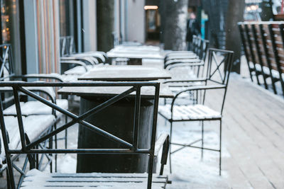 Empty chairs and tables at sidewalk cafe against buildings in city