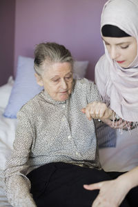 Senior woman being assisted by female home caregiver in bed