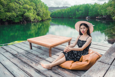 Portrait of woman sitting on wood against lake