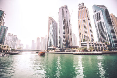 View of modern buildings by river against sky