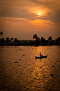 Silhouette man rowing boat on lake against sky during sunset