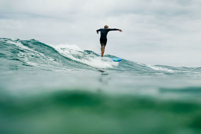 Rear view of man surfing on sea against sky