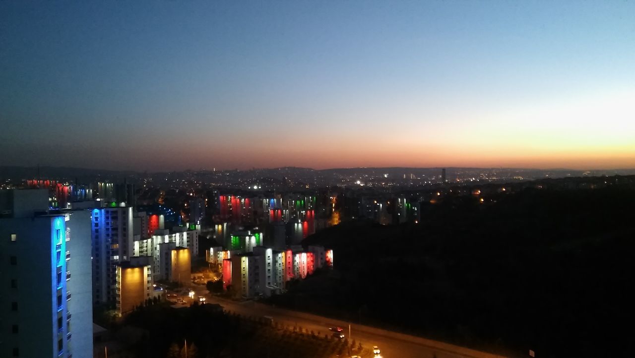 copy space, illuminated, city, clear sky, cityscape, architecture, built structure, building exterior, blue, crowded, sky, outdoors, dark, scenics, office building, residential district, city life, skyscraper, no people, aerial view, horizon over land, development, tranquility, beauty in nature